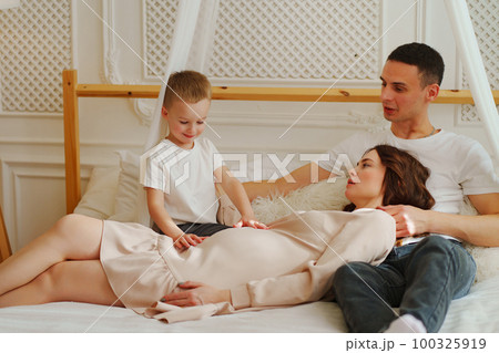 Happy pregnant mom, dad and son play in bed. the concept of family happiness. Happy pregnant mom, dad and son play in bed. the concept of family happiness. 100325919