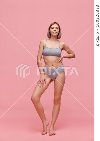 Portrait of young thin sportive woman in grey cotton inner wear posing over pink background. Concept of natural beauty, body and skin care, healthy eating 100326333