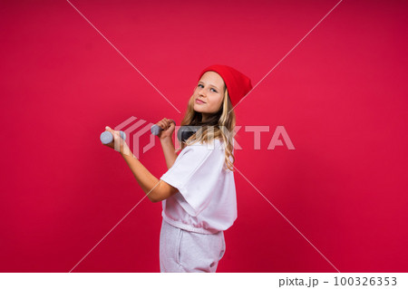 Kid girl doing fitness exercises with dumbbells on red background 100326353