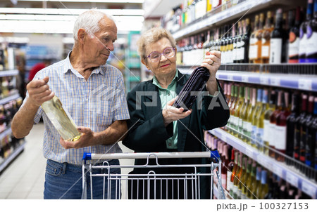 mature couple chooses bottle of wine in alcohol section of supermarket mature couple chooses bottle of wine in alcohol section of supermarket 100327153