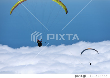 Flight above the clouds, paragliders are flying on a paraglider in the sky. Tandem flight above the clouds Flight above the clouds, paragliders are flying on a paraglider in the sky. Tandem flight above the clouds 100328662