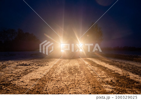 Yellow headlight and dirtroad in the dark after snowing. Car driving on a dangerous road in dire Yellow headlight and dirtroad in the dark after snowing. Car driving on a dangerous road in dire 100329025