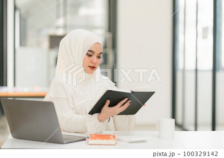 In the office, a Muslim businesswoman wearing a hijab is diligently working at her computer, displaying professionalism and commitment to her job. 100329142