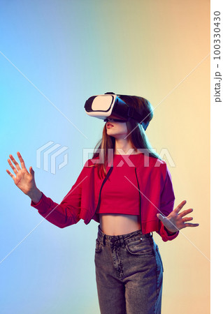 One teen girl wearing VR headset glasses over gradient blue-yellow background. Youth and virtual lifestyle of future. Concept of games, digitalization and technology 100330430