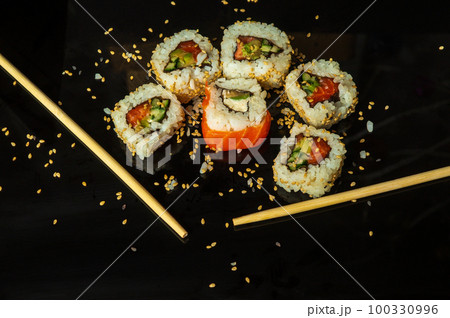 Traditional sushi with sesame seeds and chopsticks - Philadelphia with salmon, avocado and cheese. Japanese cuisine on black background Traditional sushi with sesame seeds and chopsticks - Philadelphia with salmon, avocado and cheese. Japanese cuisine on black background 100330996