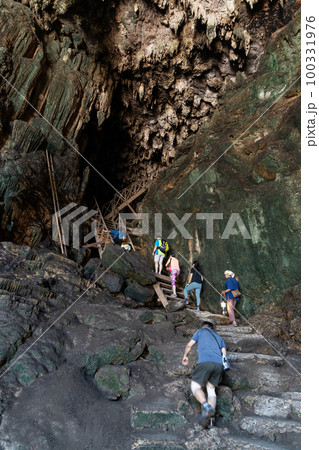 Local tour guide with traditional lantern guiding tourists through the tall and dark chambers of Tham Nam Lod caves Local tour guide with traditional lantern guiding tourists through the tall and dark chambers of Tham Nam Lod caves 100331976