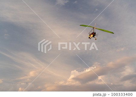 Propeller plane flies in the sunset sky. A small private hang-glider in a cloudy sky. Propeller plane flies in the sunset sky. A small private hang-glider in a cloudy sky. 100333400