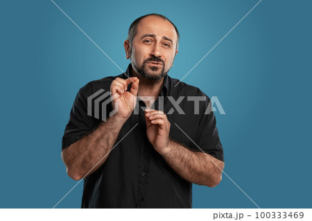 Close-up portrait of a brunet middle-aged man with beard, dressed in a black t-shirt and posing against a blue background. 100333469