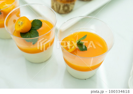 Tangerine panna cotta decorated with kumquat and mint in a plastic glass. Dessert for candy bar Tangerine panna cotta decorated with kumquat and mint in a plastic glass. Dessert for candy bar 100334618