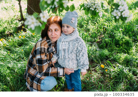Young woman with her daughter in nature admires white flowering of spring trees Young woman with her daughter in nature admires white flowering of spring trees 100334635