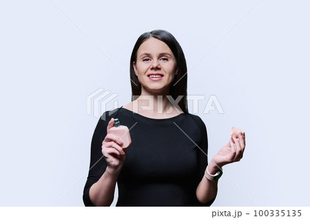 Young woman using bottle of perfume, on white studio background Young woman using bottle of perfume, on white studio background 100335135