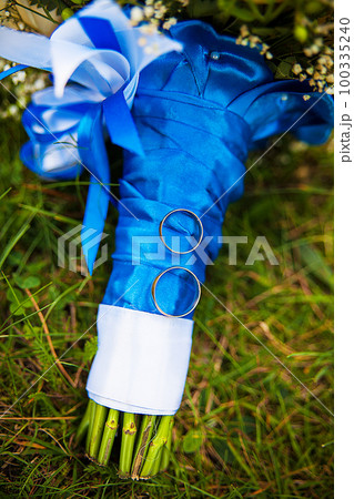 wedding rings and bridal bouquet lying on green grass 100335240