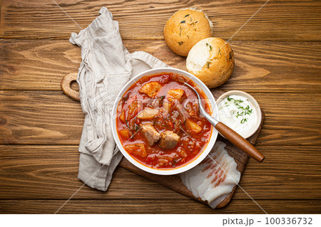 Ukrainian Borscht, red beetroot soup with meat, in white bowl with sour cream, garlic buns Pampushka and salo slices, rustic stone background. Traditional authentic dish of Ukraine Ukrainian Borscht, red beetroot soup with meat, in white bowl with sour cream, garlic buns Pampushka and salo slices, rustic stone background. Traditional authentic dish of Ukraine 100336732
