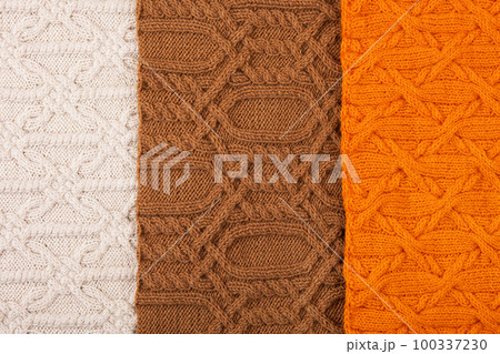 Knitted orange, brown, and beige background. Large knitted fabric with a pattern. Close-up of a knitted blanket. Banner 100337230