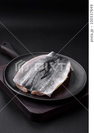Delicious salted herring fillet in oil on a black ceramic plate 100337649