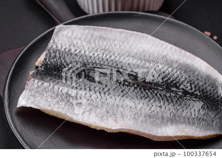 Delicious salted herring fillet in oil on a black ceramic plate 100337654