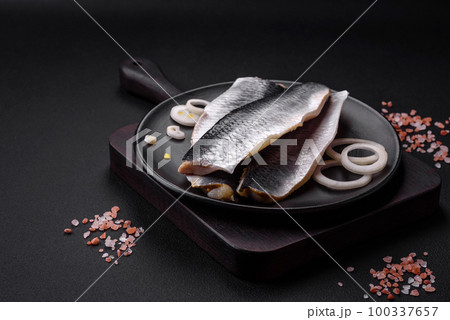 Delicious salted herring fillet in oil on a black ceramic plate 100337657