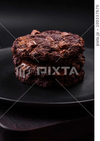 Delicious fresh oatmeal round cookies with chocolate on a black ceramic plate Delicious fresh oatmeal round cookies with chocolate on a black ceramic plate 100337670