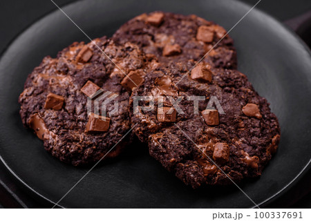 Delicious fresh oatmeal round cookies with chocolate on a black ceramic plate 100337691
