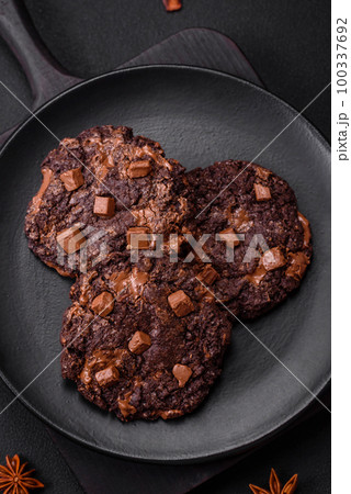 Delicious fresh oatmeal round cookies with chocolate on a black ceramic plate 100337692