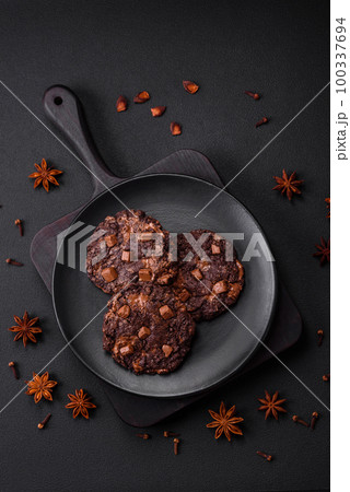 Delicious fresh oatmeal round cookies with chocolate on a black ceramic plate 100337694