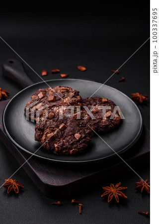 Delicious fresh oatmeal round cookies with chocolate on a black ceramic plate Delicious fresh oatmeal round cookies with chocolate on a black ceramic plate 100337695