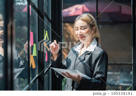 girl asian woman entrepreneur of small company putting a adhesive sticky notes in glass wall in office during analyzing formulating business strategies girl asian woman entrepreneur of small company putting a adhesive sticky notes in glass wall in office during analyzing formulating business strategies 100338191