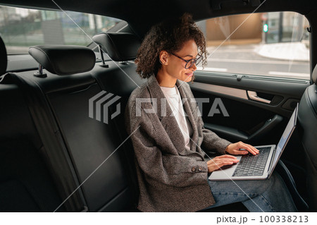 Executive woman manager working on laptop sitting car leather backseat on the way to office 100338213