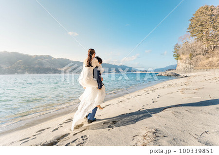 海辺の砂浜でおんぶしている新郎新婦 海辺の砂浜でおんぶしている新郎新婦 100339851