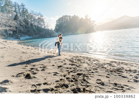 海辺の砂浜でおんぶしている新郎新婦 100339862