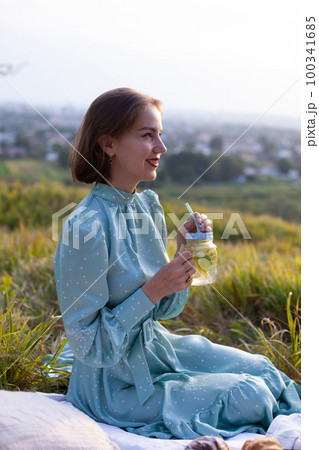 A woman in blue dress sits on a picnic in a park with panoramic view A woman in blue dress sits on a picnic in a park with panoramic view 100341685