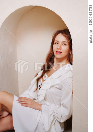 a woman in a white dress barefoot sitting on the floor in an arch on the wall a woman in a white dress barefoot sitting on the floor in an arch on the wall 100343755