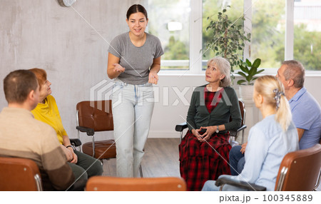 Young female tutor communicating with elderly people in language club 100345889