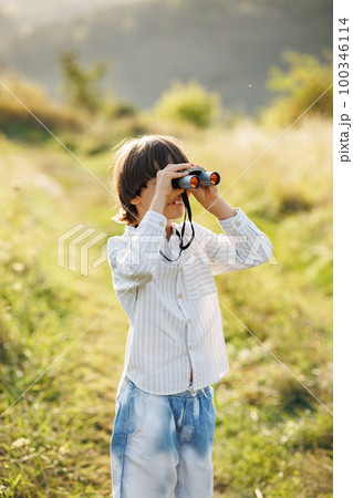Portrait of little explorer with binoculars in a field. Little caucasian boy looking through a binoculars in a field at summer. Brunette boy wearing striped shirt. Portrait of little explorer with binoculars in a field. Little caucasian boy looking through a binoculars in a field at summer. Brunette boy wearing striped shirt. 100346114