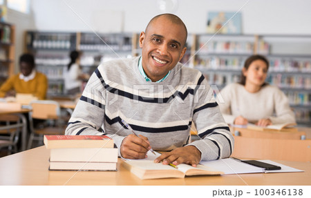 Cheerful adult hispanic student studying in university library 100346138