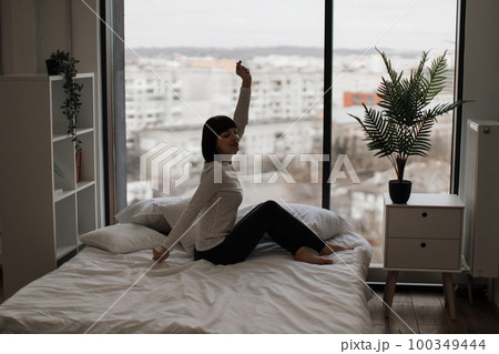 Pleasant woman stretching arms on white comfy bed 100349444