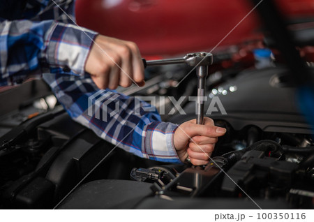 Female auto mechanic unscrewing a nut to replace a car spark plug. Female auto mechanic unscrewing a nut to replace a car spark plug. 100350116