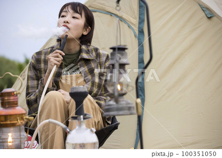 焚火をしながらで水タバコを吸う若い女性 シーシャ 焚火をしながらで水タバコを吸う若い女性 シーシャ 100351050