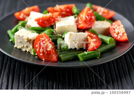 Green beans salad with feta on a black plate. Plate with delicious green beans salad on wooden table, closeup. 100356997