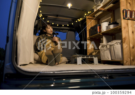 夜のオートキャンプ場で車の中で寛ぐ若い女性　車中泊イメージ 100359294