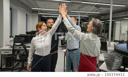 Four co-workers give a high five in the office. Four co-workers give a high five in the office. 100359452