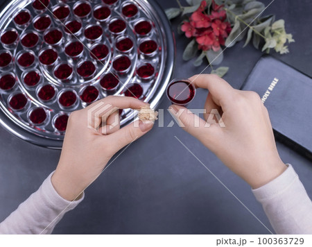 Closeup of young woman taking communion from small cups on black background 100363729