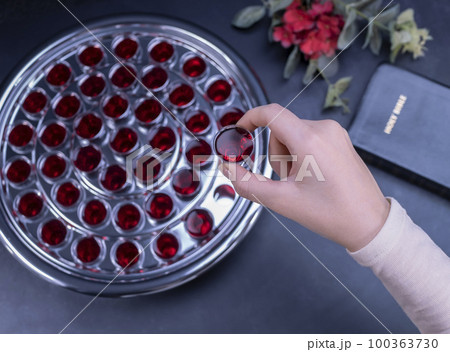Closeup of young woman taking communion from small cups on black background 100363730