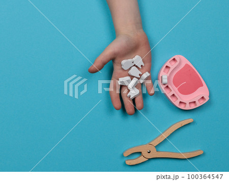 Dentist game. A child's hand holds toy wooden teeth. A toy jaw without teeth and forceps for removal nearby. Dentist game. A child's hand holds toy wooden teeth. A toy jaw without teeth and forceps for removal nearby. 100364547