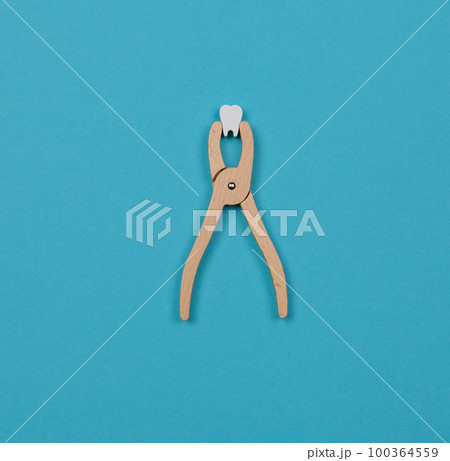 Children's dental play set. Wooden tongs with a toy tooth. Blue background, copy space Children's dental play set. Wooden tongs with a toy tooth. Blue background, copy space 100364559