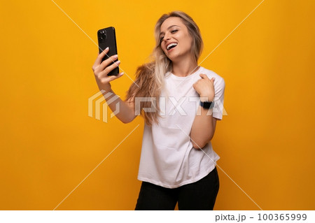 a girl with a phone in her hands takes a photo on a yellow background 100365999