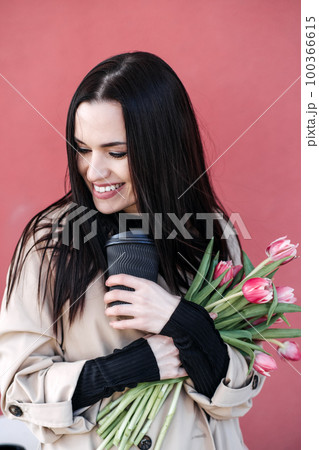 Spring outdoor portrait of happy woman with tulips bouquet and coffee to go on spring city street. Happy young woman holding bouquet of pink flowers Spring outdoor portrait of happy woman with tulips bouquet and coffee to go on spring city street. Happy young woman holding bouquet of pink flowers 100366615