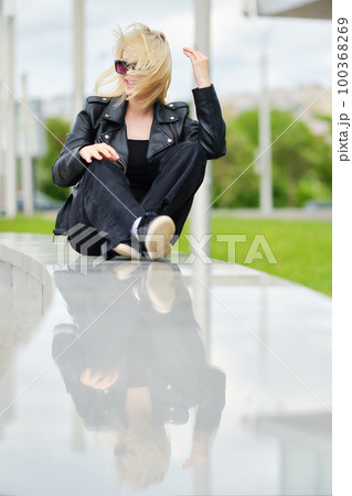 Girl in total black outfit sits on railing in windy day Girl in total black outfit sits on railing in windy day 100368269