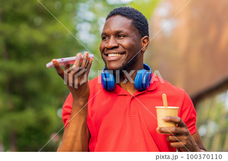 young afro american man with headphones on neck using smartphone in summer park young afro american man with headphones on neck using smartphone in summer park 100370110