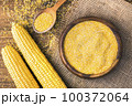 Corn grits in a wooden bowl on the background of fresh corn on the cob on a burlap. 100372064